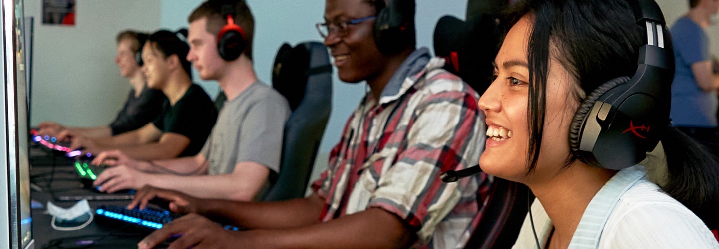row of smiling students playing PC esports with headsets