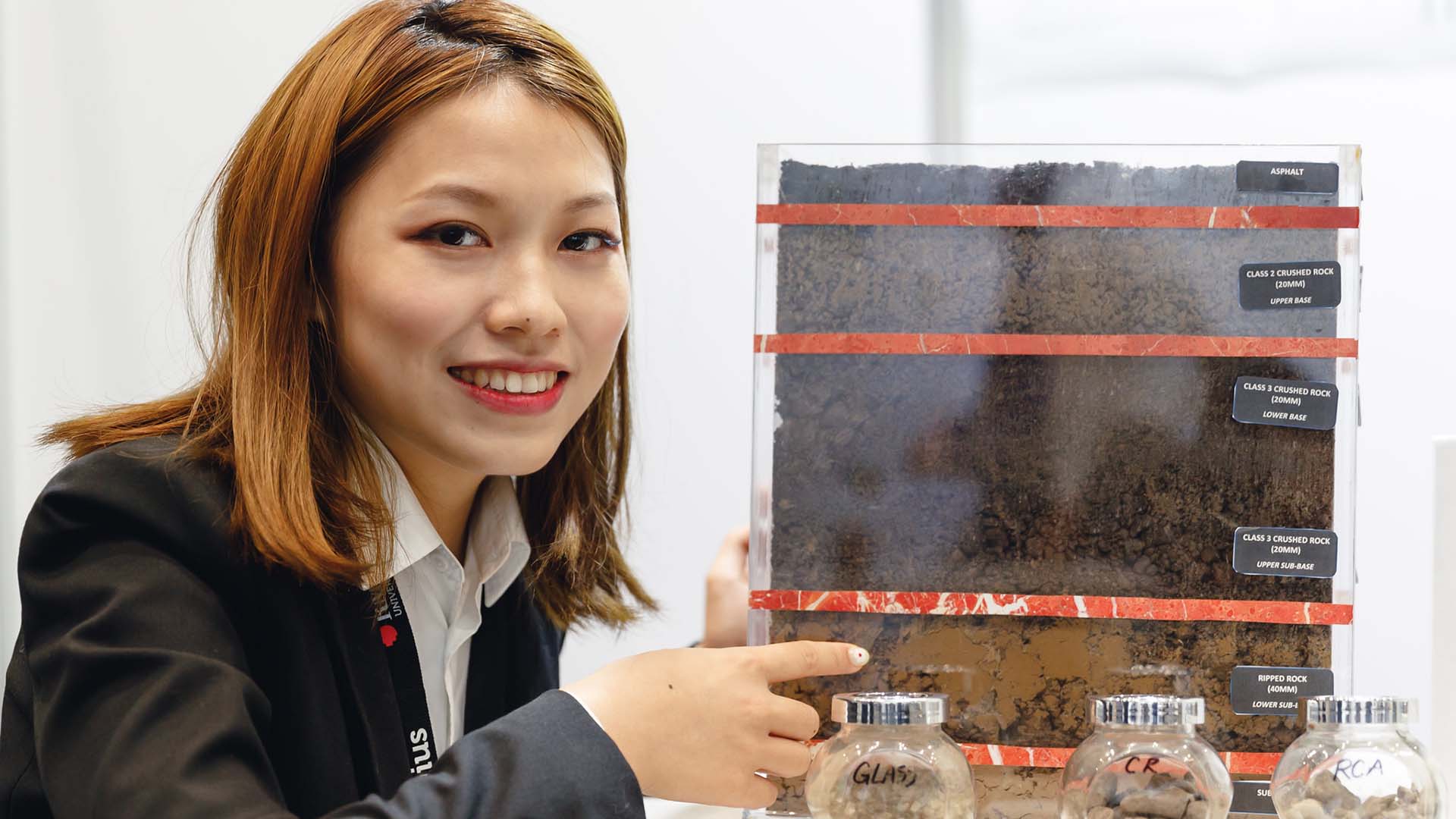 Female student in business clothes showing  display of soil layers