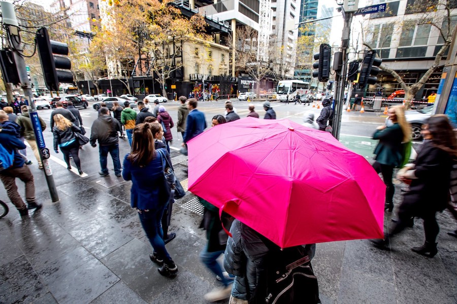 pedestrians crossing a wet street in melbourne, with one person holding a bright pink umbrella in the foreground