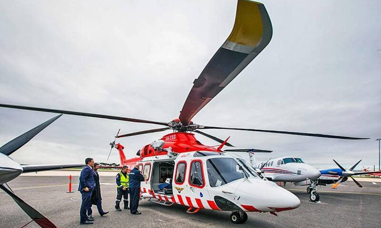 a medical helicopter sits on the tarmac with several men standing nearby