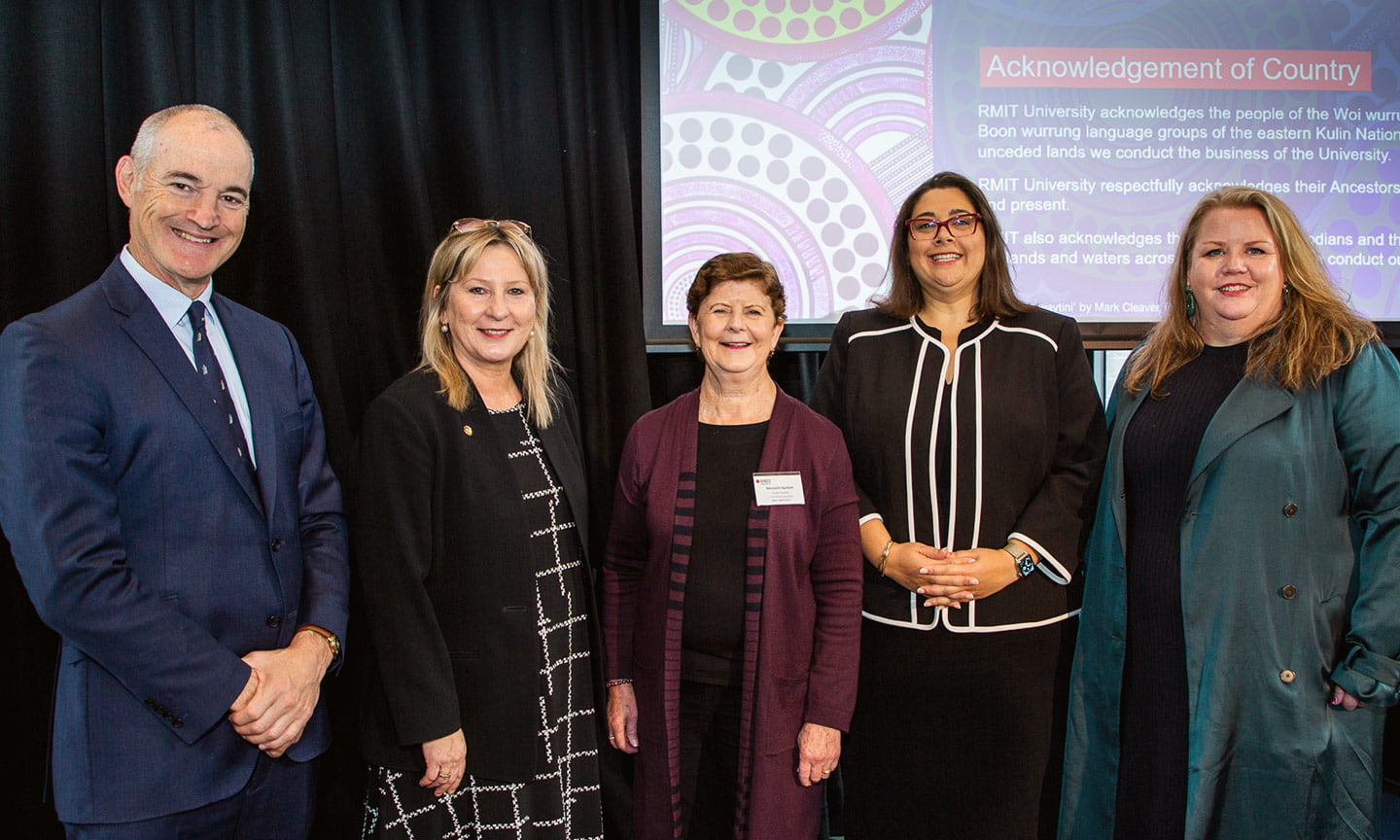 RMIT Vice-chancellor Alec Cameron, Victorian Minister for Training and Skills Gayle Tierney and several others stand together in front of a presentation.