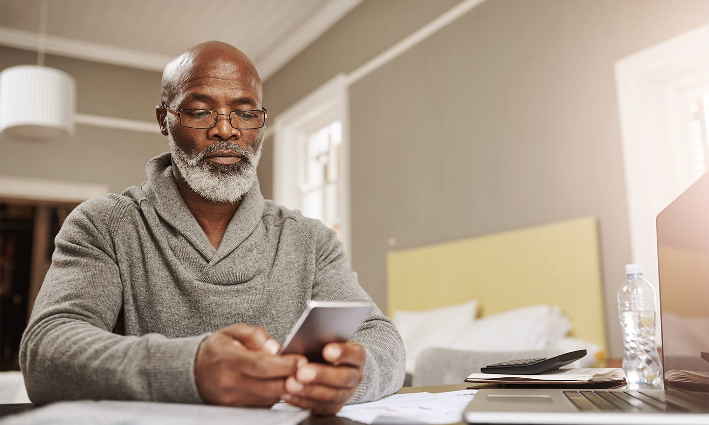 Man sitting at a desk in a grey sweater using a mobile phone.