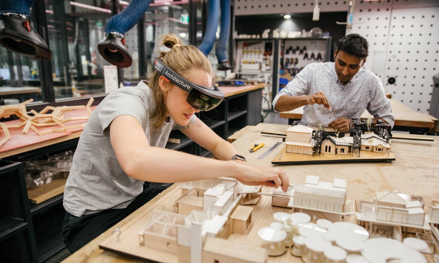 Two students working on architectural models, one using a wrap around headset.