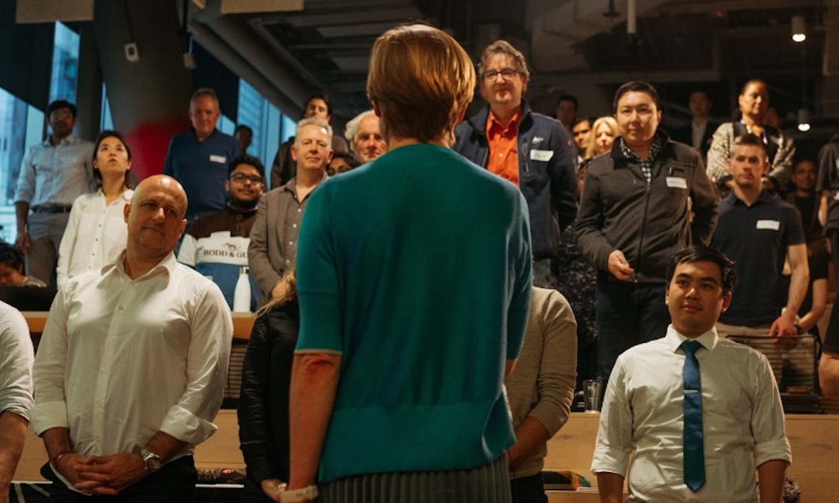 a woman giving a presentation to a group of people, photo is taken from behind her point of view