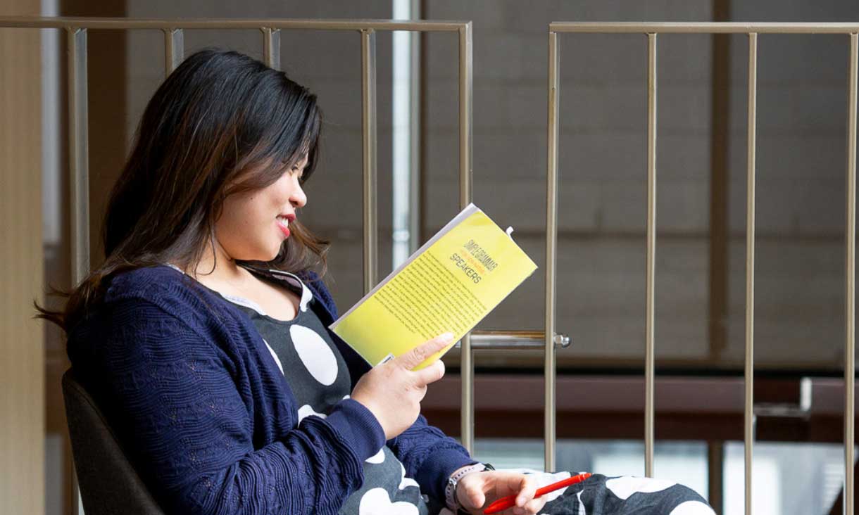 A young woman reads a yellow book in a chair at Swanston Library