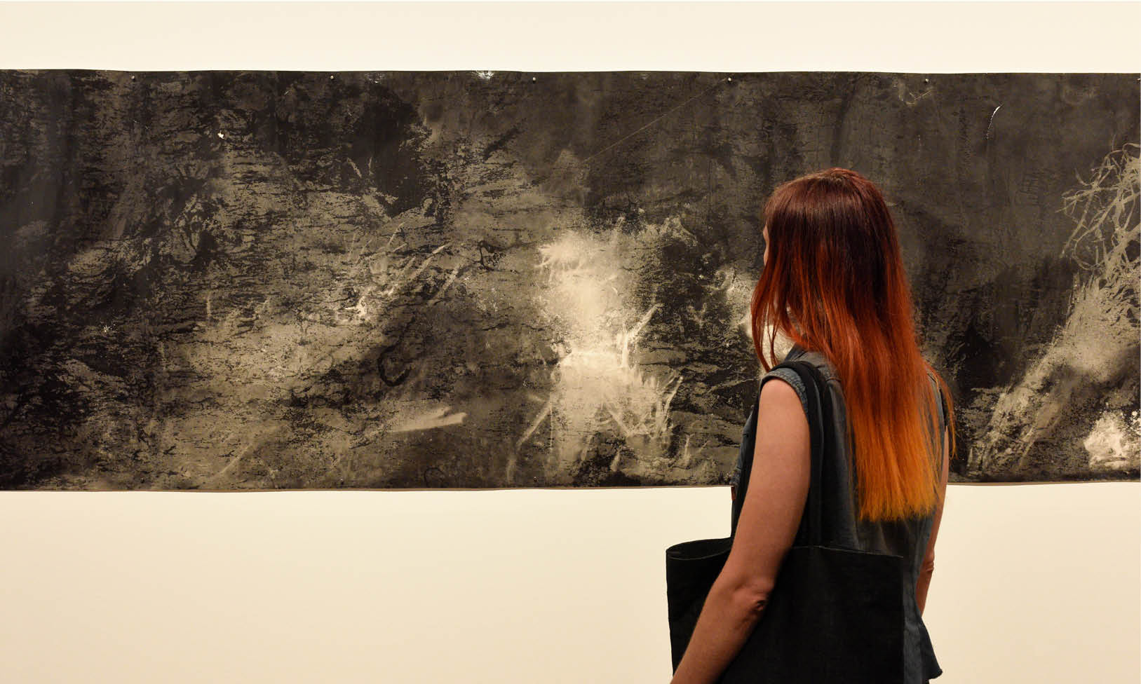 A black and white artwork a gallery. A person with orange hair is looking away from the camera towards the painting.