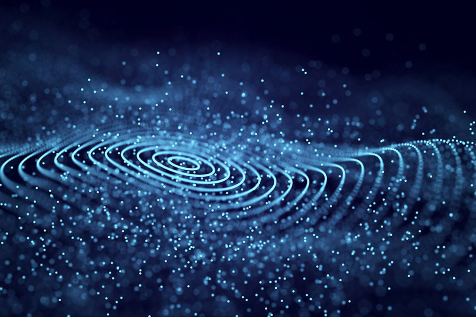Abstract image of glowing blue particles forming circular wave patterns on a dark background.