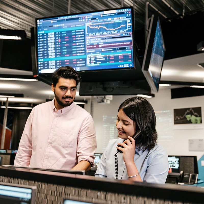 Two people with stock exchange information on a screen behind them