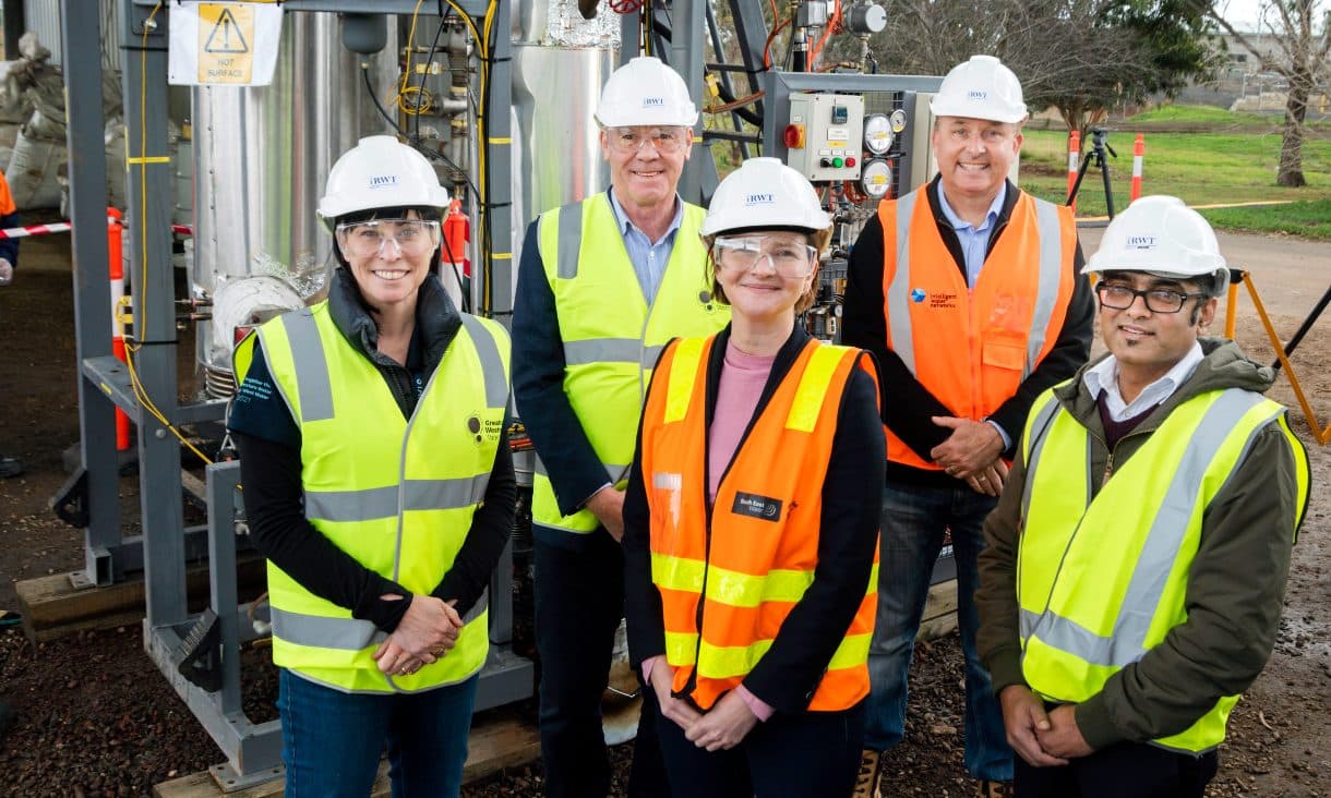 Group of people in construction clothes smiling in front of machinery