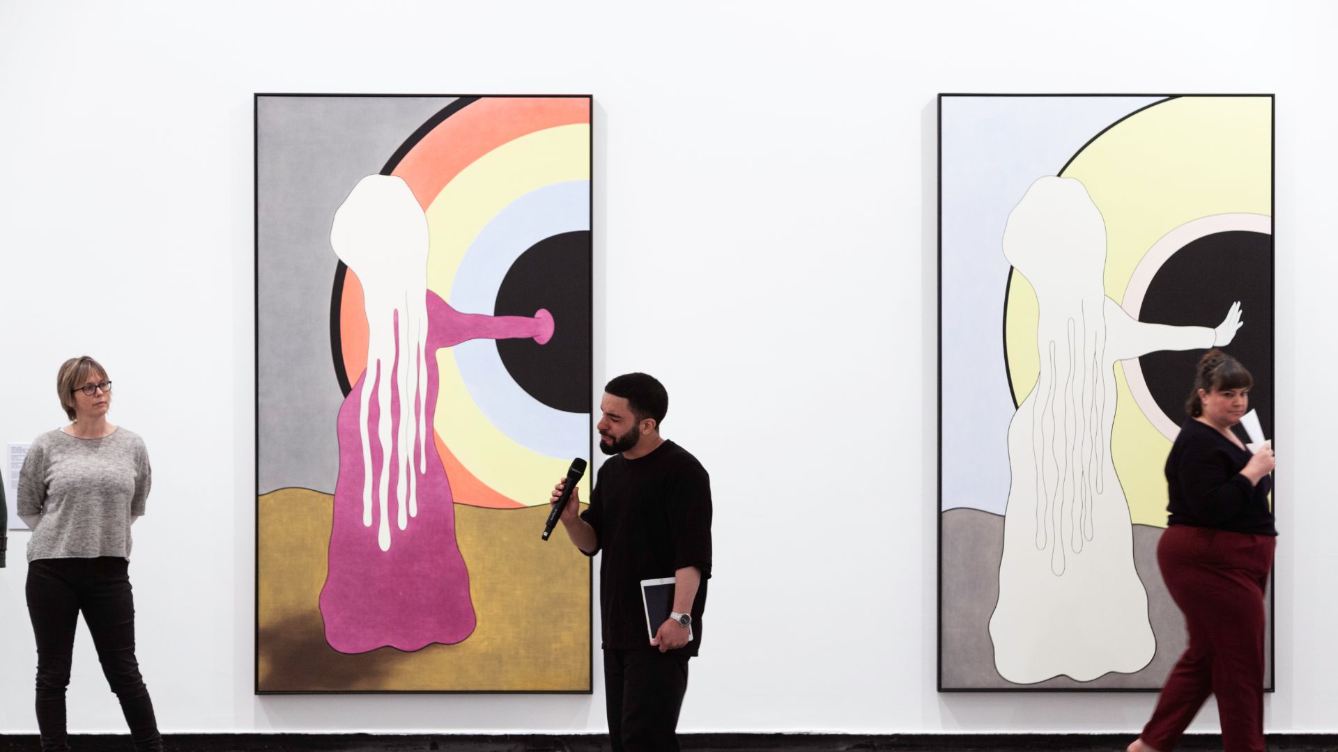 Person talking into microphone in front of two artworks in gallery