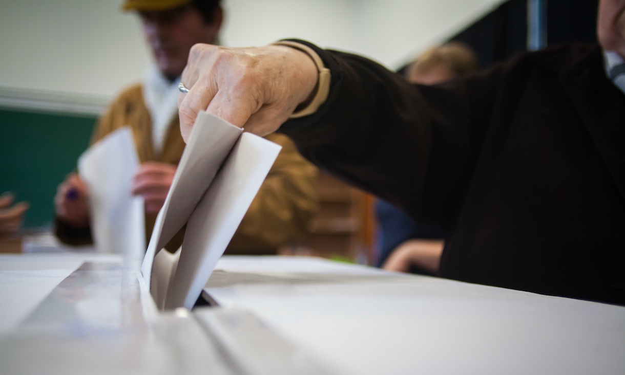 elderly person putting a folded vote into a ballot box