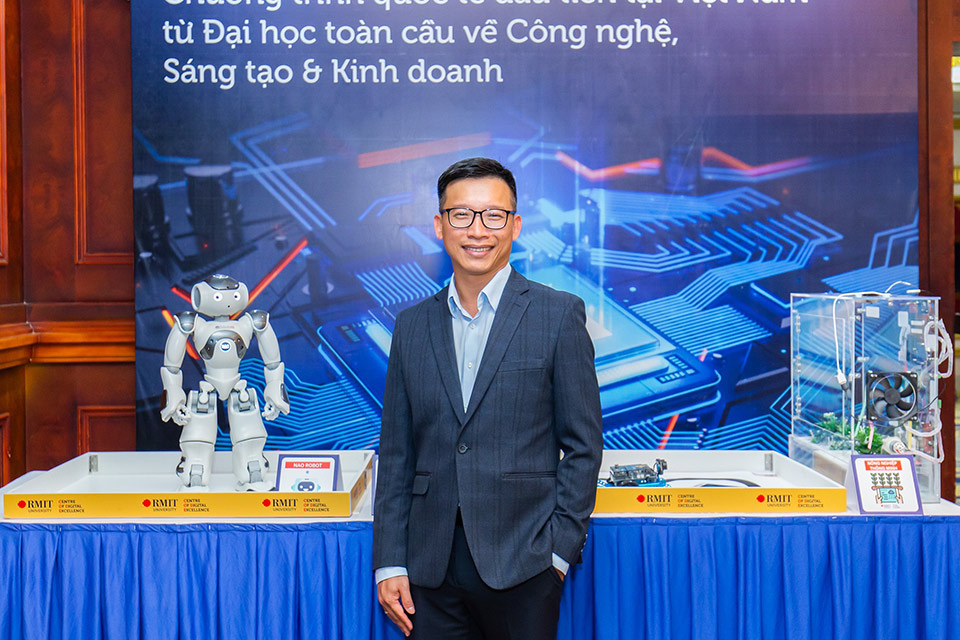 Minh Ngoc Dinh standing in front of a blue table with a robot sitting on it. 
