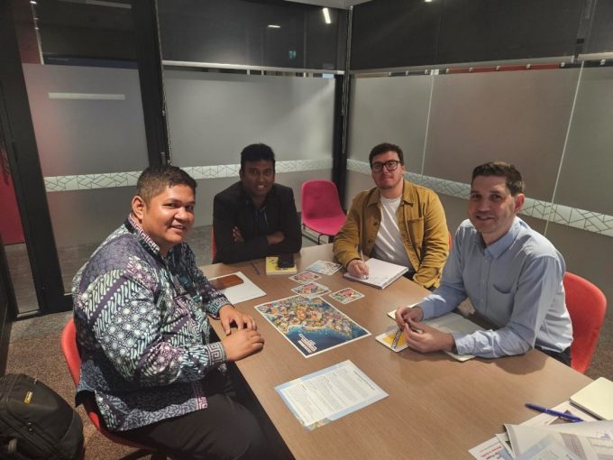 Four people sitting around a table in a meeting, looking at the camera and smiling.