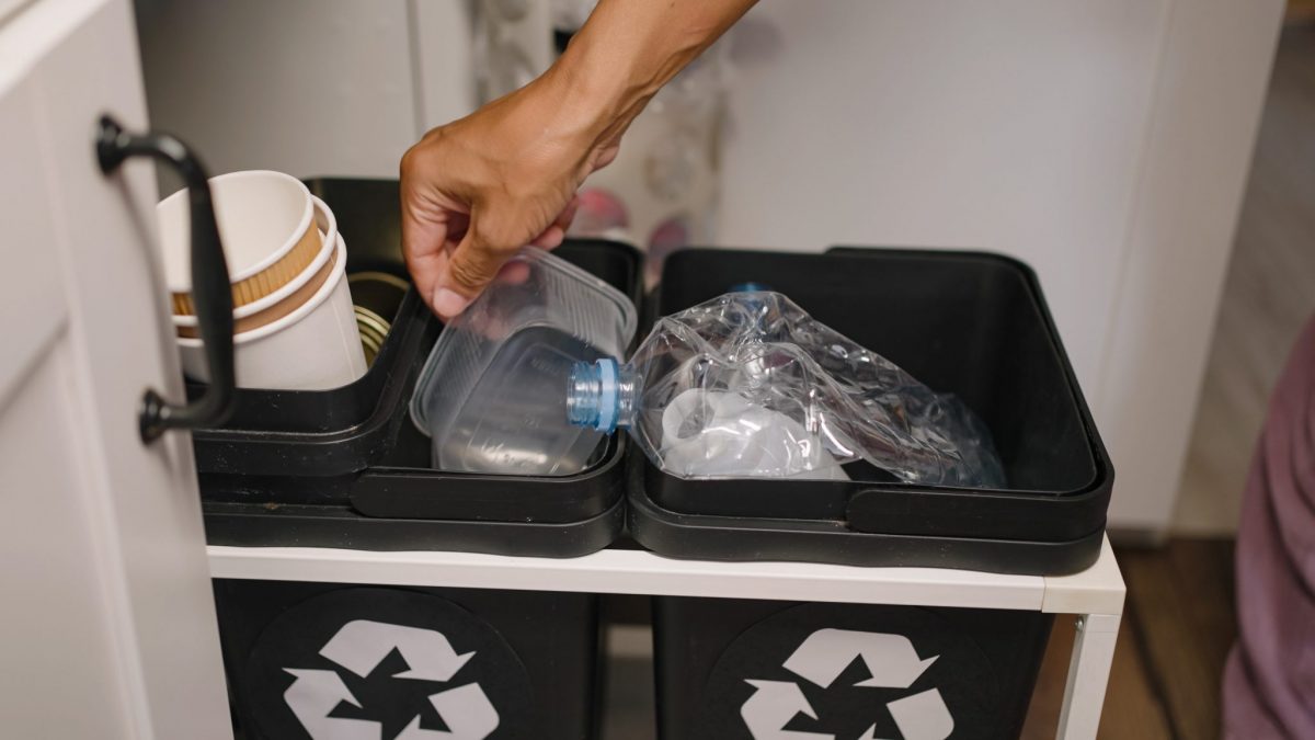 A hand putting a plastic container into a recycling bin.