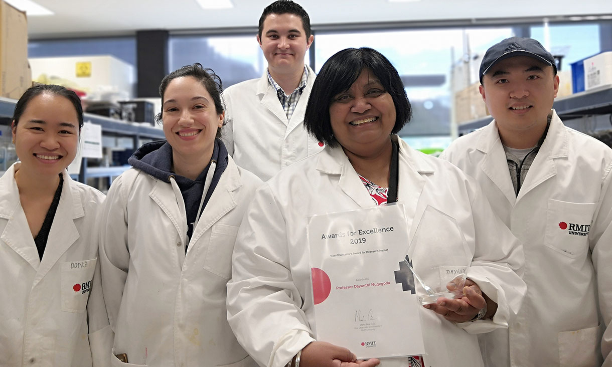 Photo of five researchers (four in front and one standing behind) standing in a laboratory wearing laboratory coats. One researcher, Professor Dayanthi Nugegoda, is holding a piece of paper representing a received award.