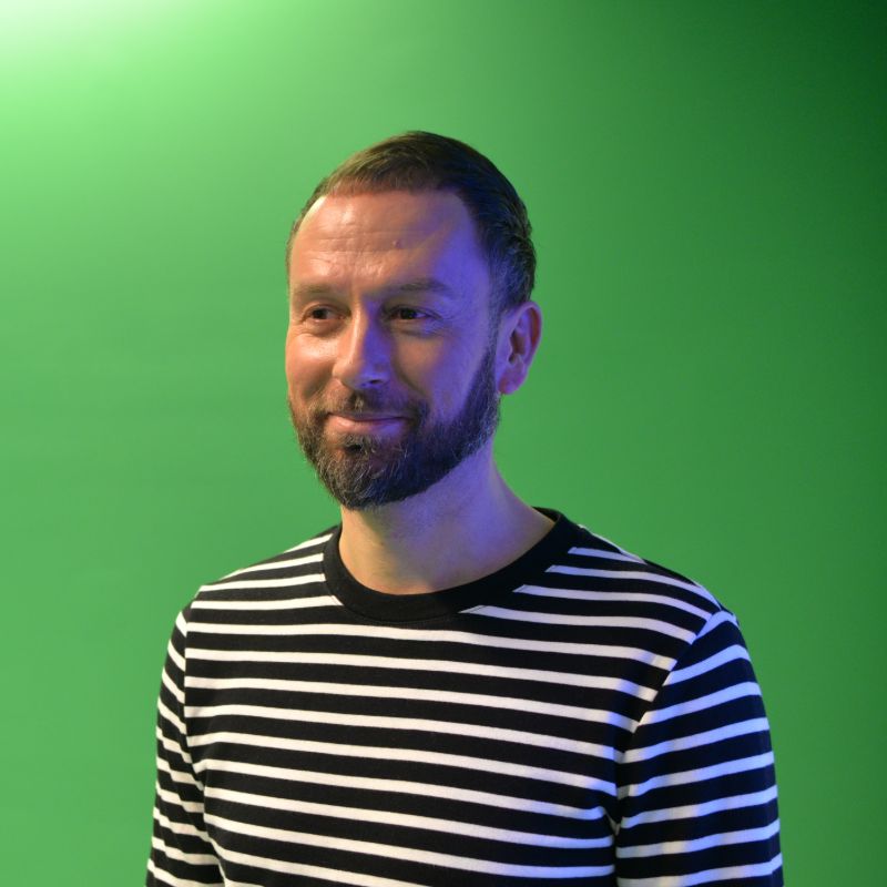 Profile photo of Cameron Duff standing in front of a green screen, looking to the left of the camera and smiling.