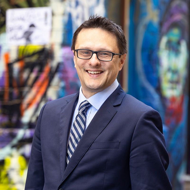 A portrait of David Smith in a city laneway with graffiti artwork behind him