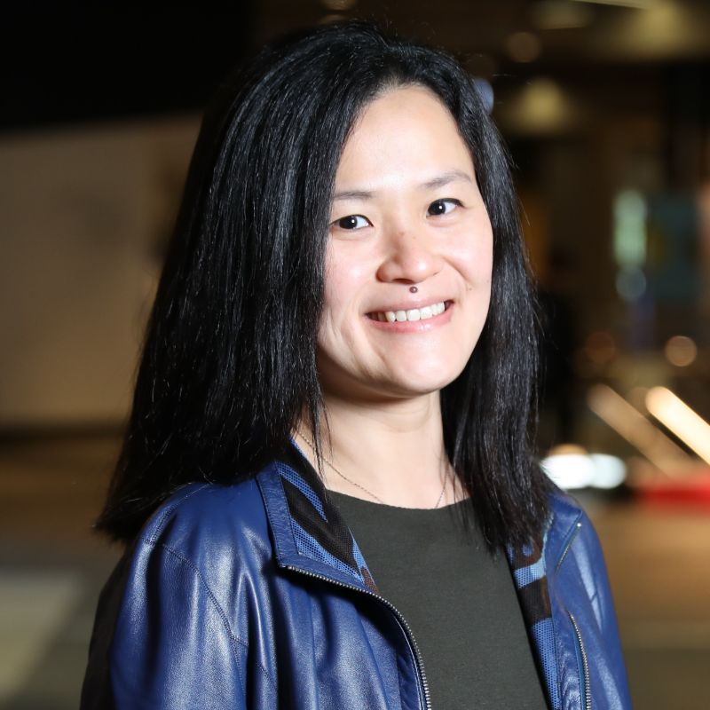 Profile photo of Flora Salim smiling towards the camera against an out of focus background. Flora is wearing a black shirt with a blue jacket.