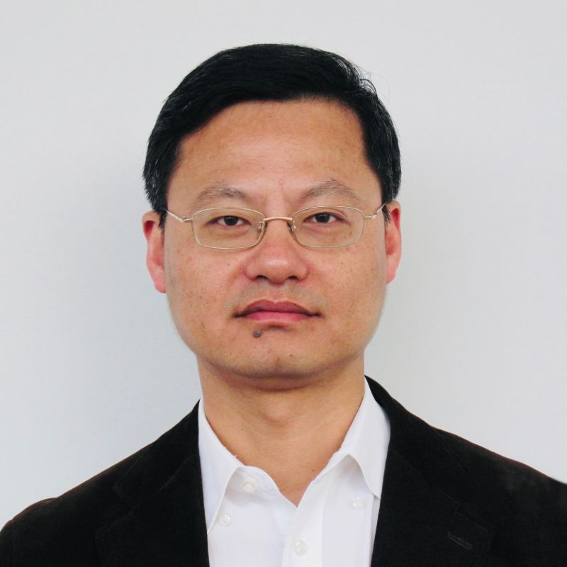 Profile photo of Professor Jie Yang. Jie is standing in front of a grey wall, looking at the camera. Jie is wearing glasses, a white button up shirt and a black blazer.