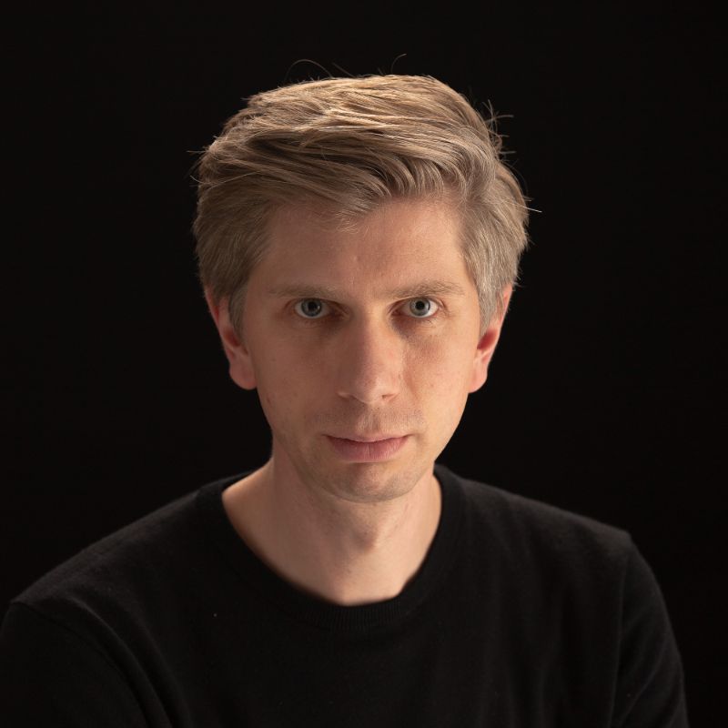 Profile photo of Martin Reftel looking towards the camera wearing a black shirt against a black background
