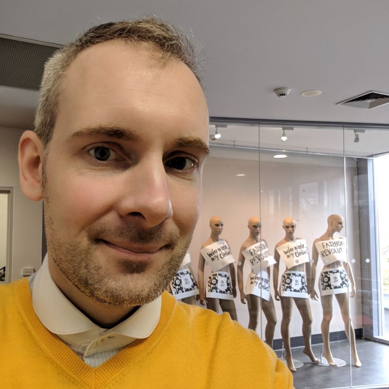 Profile photo of Dr Stephen Wigley standing inside and smiling at the camera. Behind Stephen is a glass wall displaying five mannequins wearing the same dress.