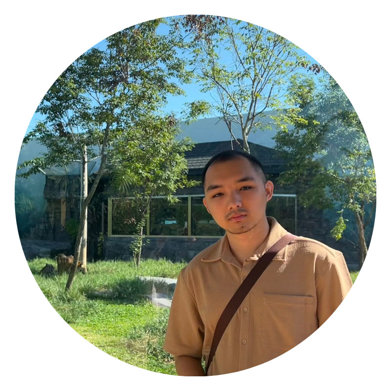 Male student in short sleeve shirt standing in front of grey building.
