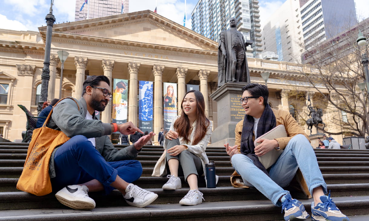 Three students sitting in front of a stately building