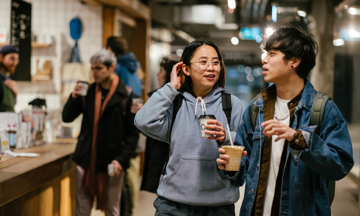 Two students holding coffee walking and talking