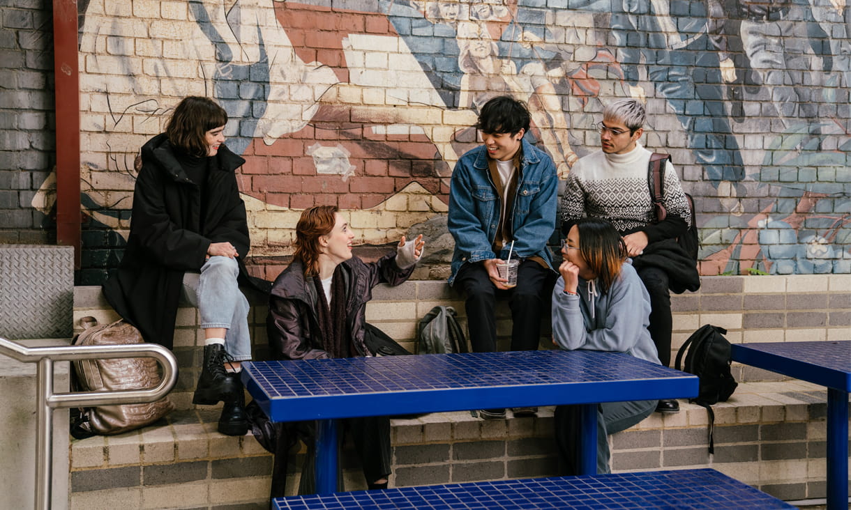 Five students sitting in front of a mural 