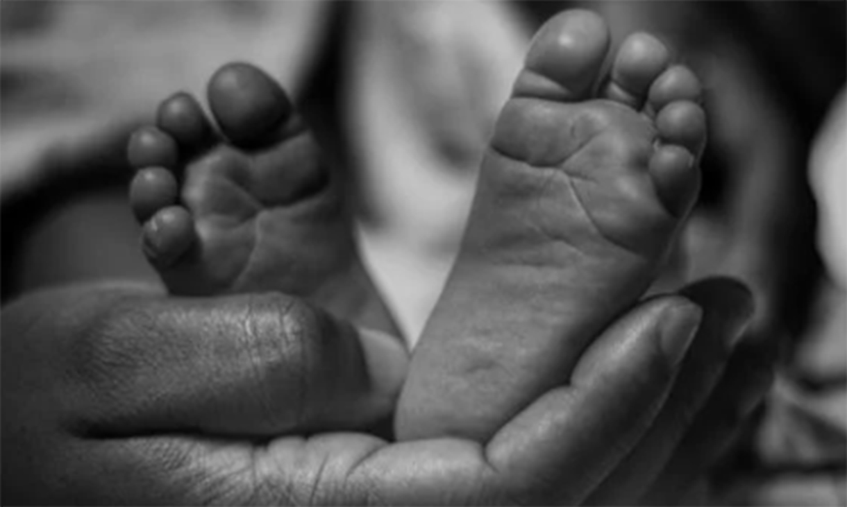 Black and white photo of a newborn’s feet being gently cradled by adult hands.