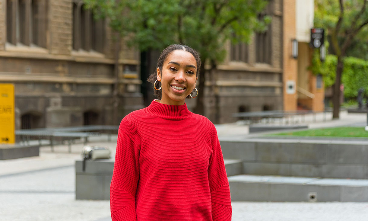 A smiling individual in a red shirt standing on RMIT campus