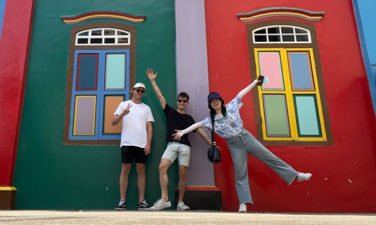 Three students pose in front of a coloured wall