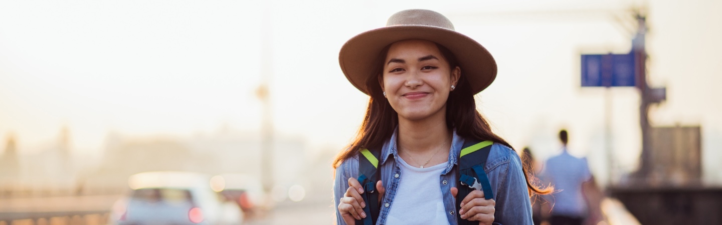Young woman wearing a wide brimmed hat and backpack smiles at the camera