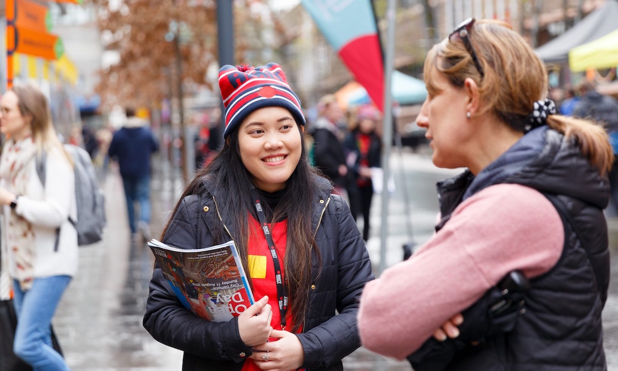 A volunteer wearing a beanie talks to a campus visitor.