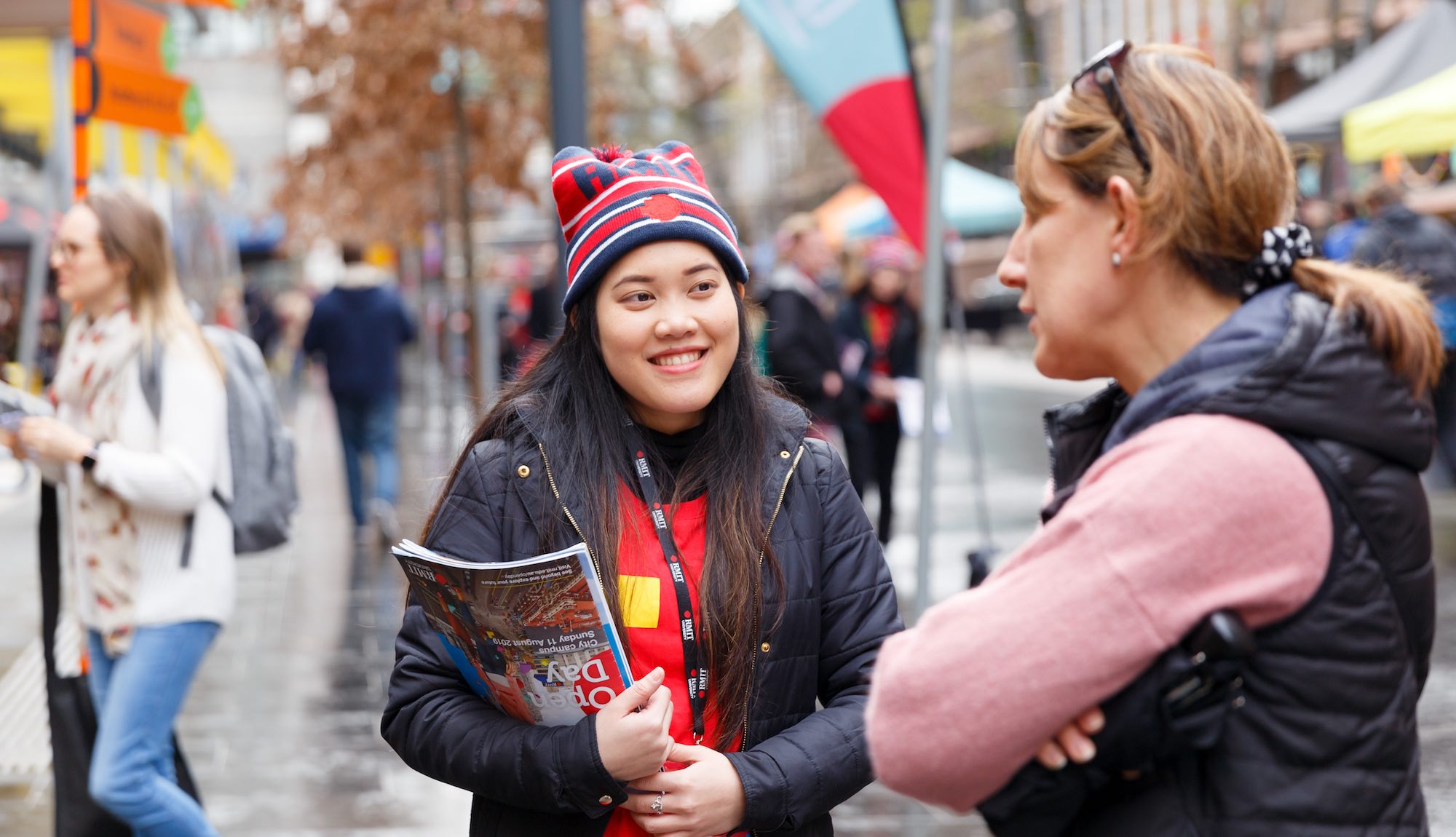 A student volunteer wearing RMIT merchandise chats to a parent at Open Day at the City Campus.