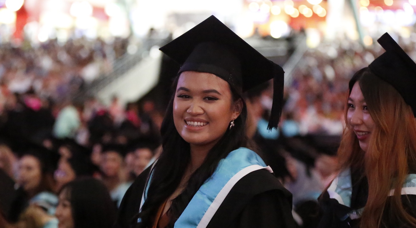 A student wearing a black and light by graduation smiles at the camera.