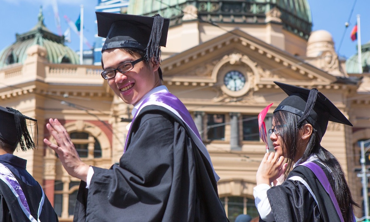 A student waves to the camera in front of Flinders St Station.