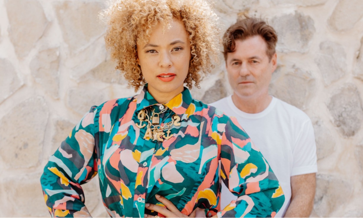The band members of Sneaky Sound System stand in front of a stone wall.