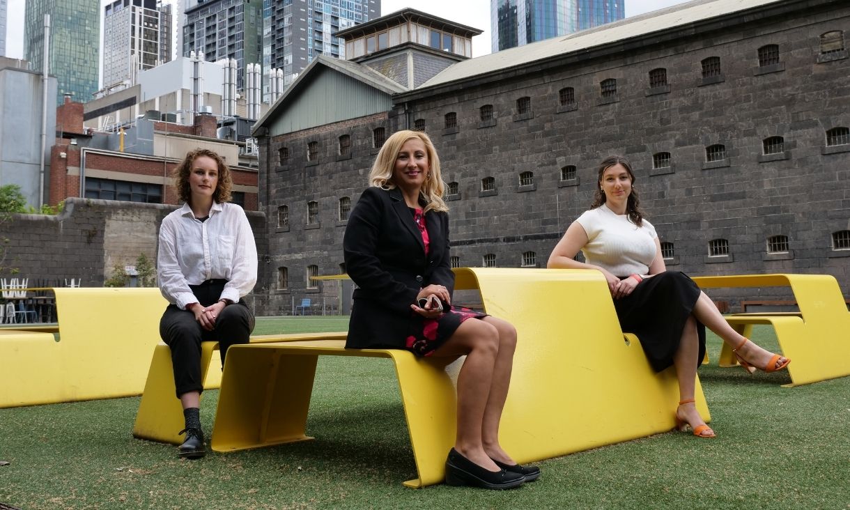 Three women sit in an RMIT courtyard and smile at the camera.