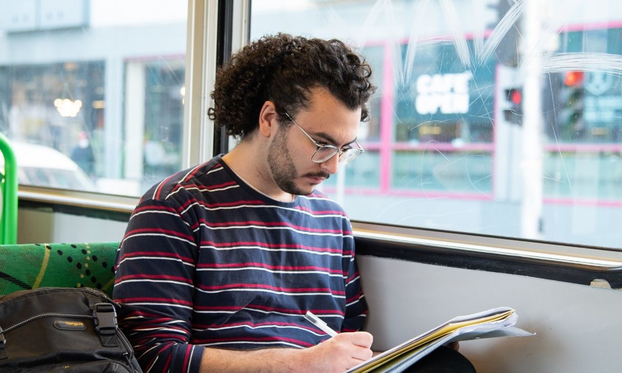 A man writes in a book on a tram.