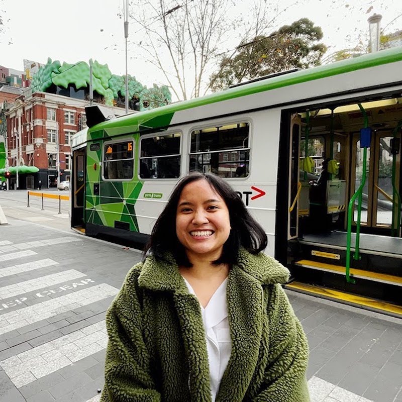 Student smiling as she stands at a tram stop.