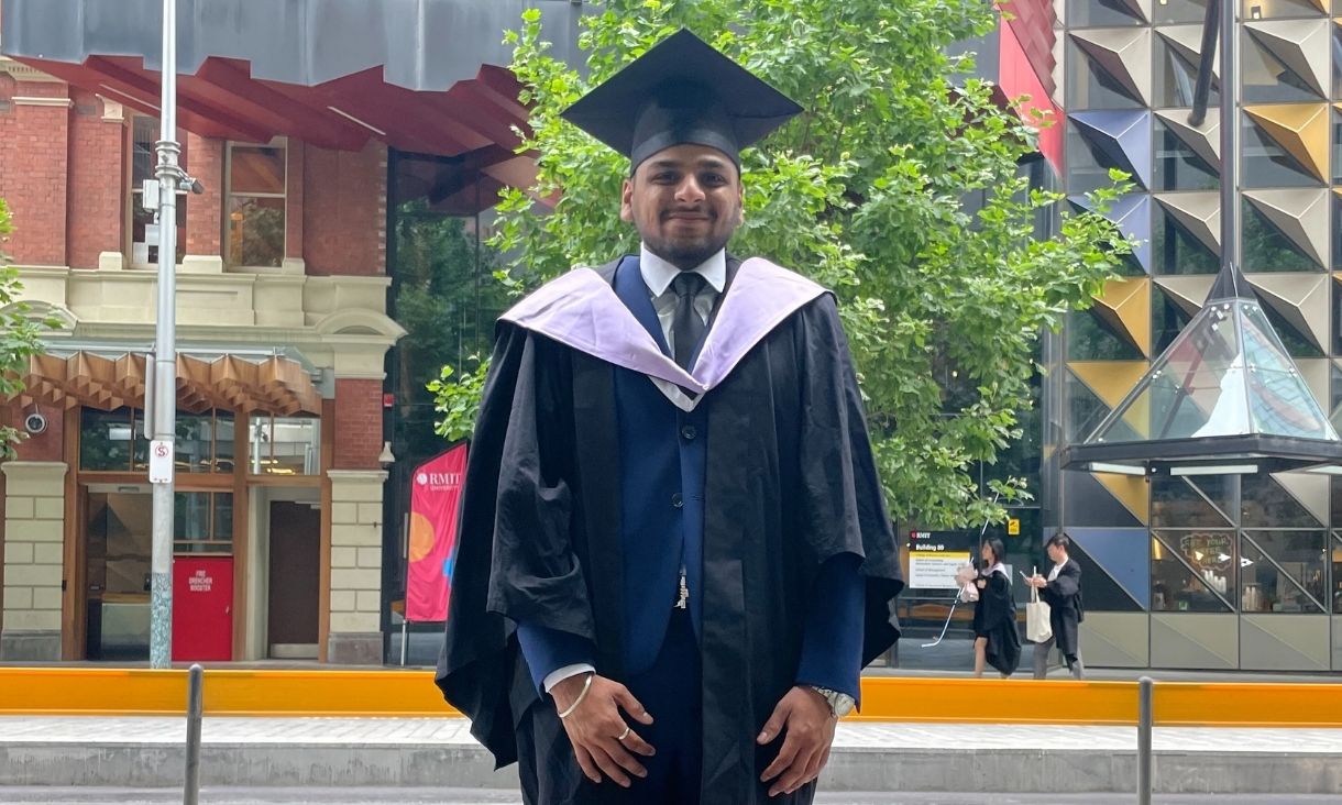 RMIT Graduate Harsh Jain in graduate cap and gown in front of RMIT building. 