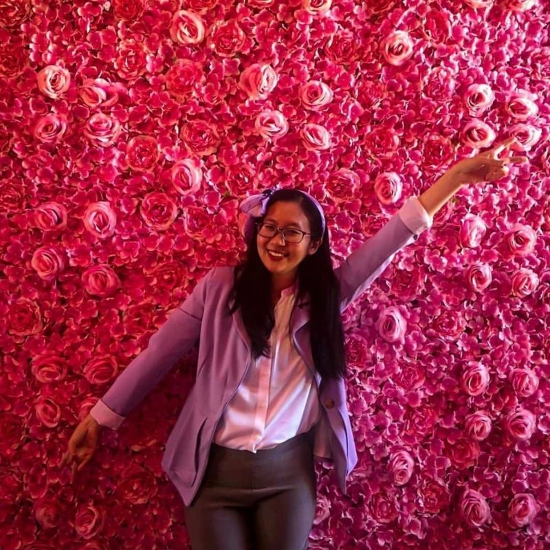 Profile photo. Woman standing in front of a wall of pink roses.