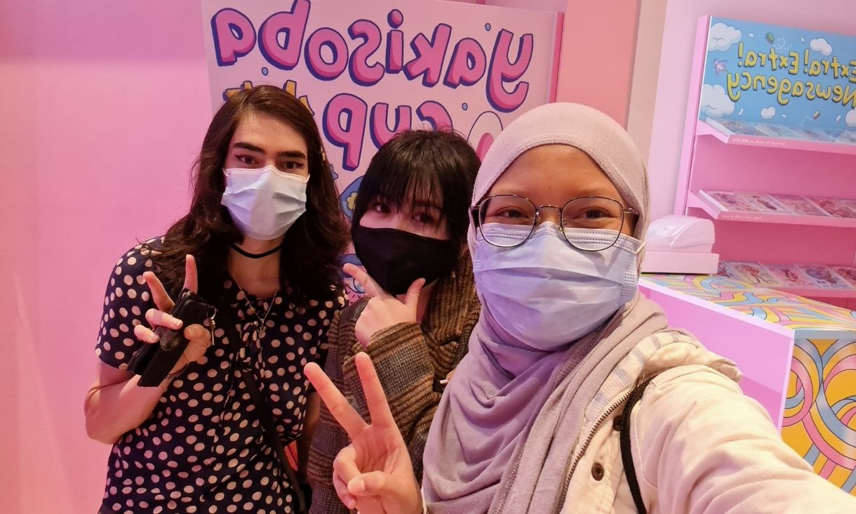 Three young students wearing masks posing for the camera in pink retail store