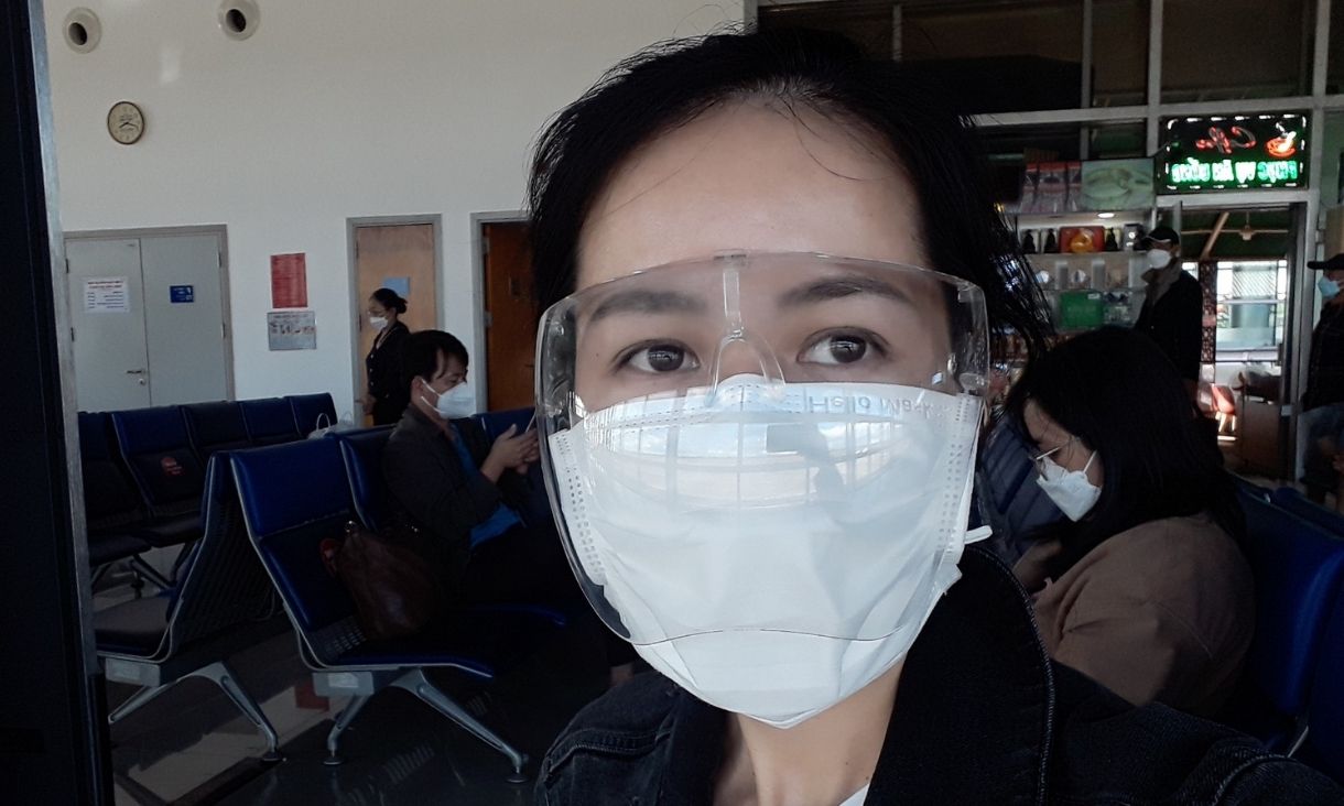 A woman in a face mask takes a selfie in an airport.