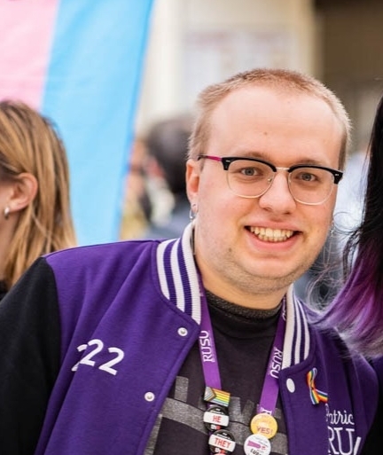 Image of young student Patrick looking at camera smiling wearing purple jacket 