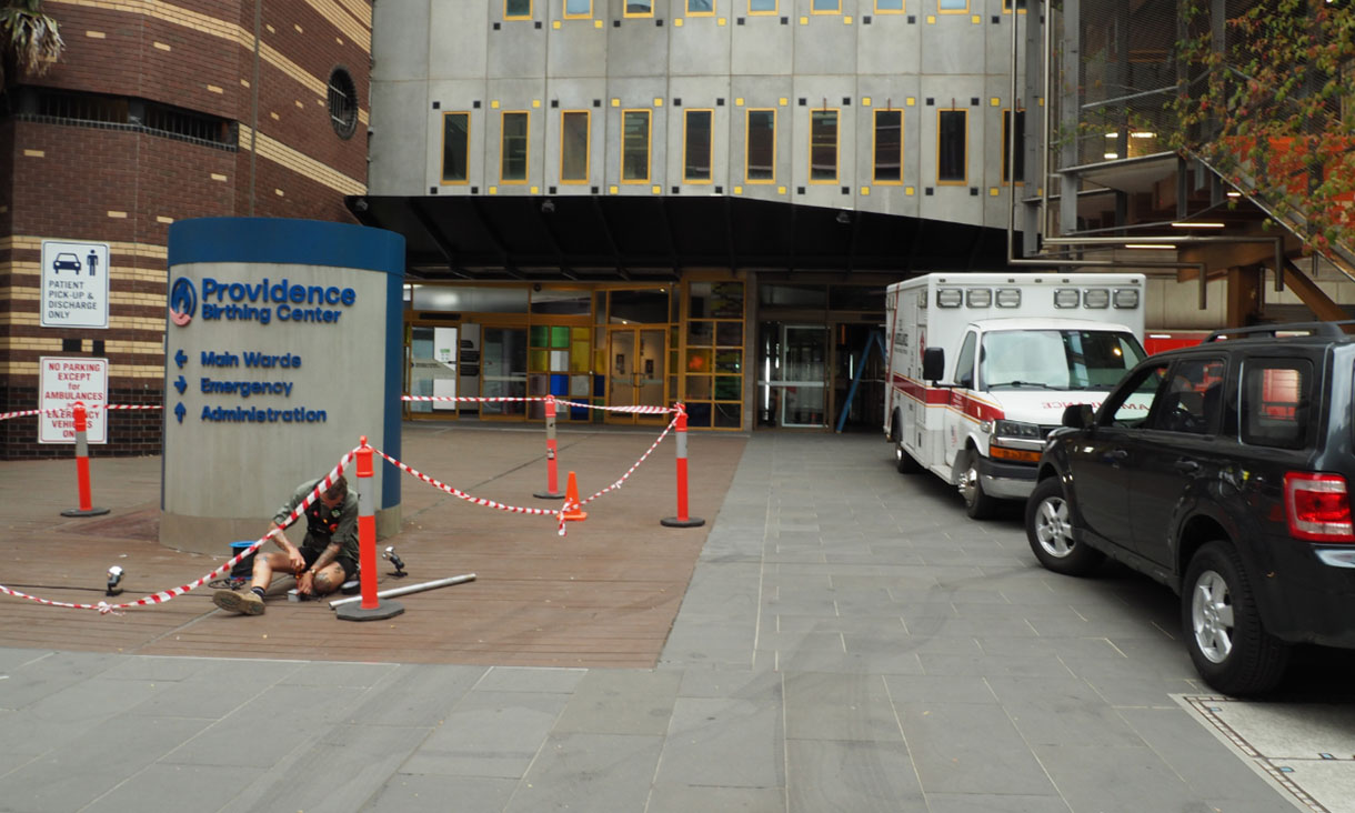 A sign reading ‘Providence Birthing Center’ is in front of a building, with an ambulance and a car to the right
