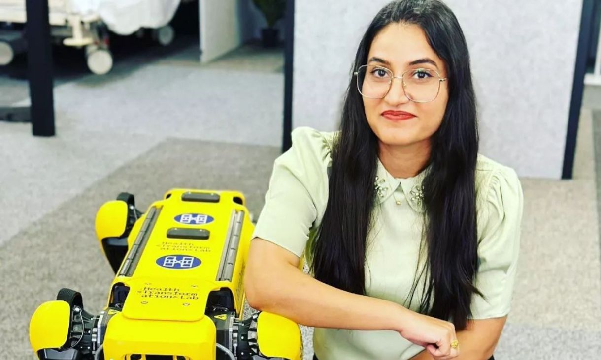 RMIT student Jyoti kneeling down beside a large yellow robot