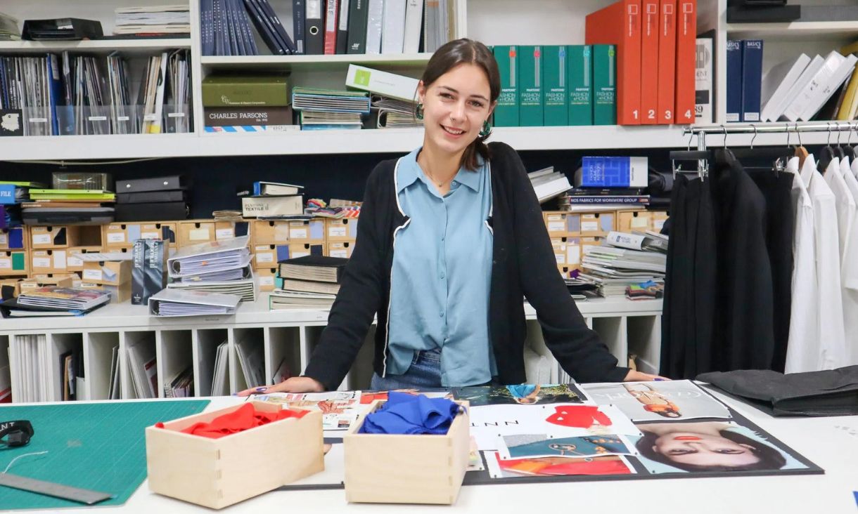 RMIT Textile design student Lucinda standing in classroom behind desk which features her textile artwork