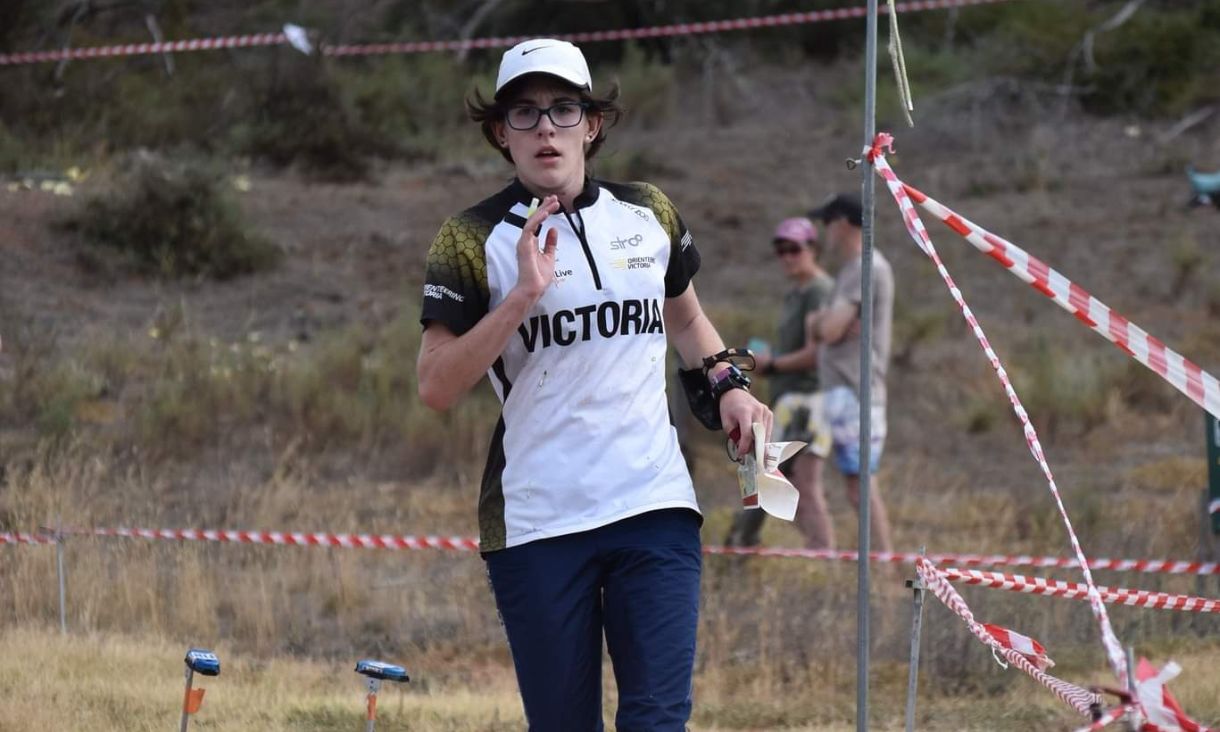 Young student running through field wearing Victoria jersey during an orienteering competition.